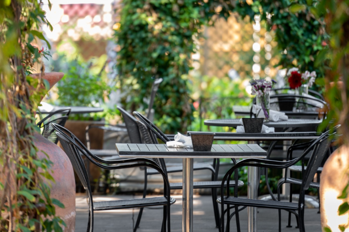 Outdoor patio at Garden Café with black metal chairs, tables set with napkins, potted plants, and lush greenery creating a cozy, garden-like dining space.